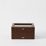 The TAWBURY Bayswater 8 Slot Watch Box with Storage in chestnut brown faux leather, featuring visible stitching, a glass top, and metal handles, is embossed with "TAWBURY" and shown against a white background.