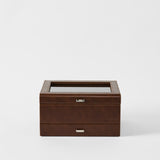 The TAWBURY Bayswater 8 Slot Watch Box with Storage in chestnut brown faux leather, featuring visible stitching, a glass top, and metal handles, is embossed with "TAWBURY" and shown against a white background.