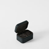 The TAWBURY Fraser 2 Watch Case in Midnight Black is a small, rectangular case with a textured finish and zipper, opening to reveal two cushioned compartments for watches.