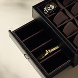 The TAWBURY Bayswater 8 Slot Watch Box with Storage in Black/Charcoal is open, elegantly displaying a watch on top, while the lower drawer stores a beige watch strap for organized storage.