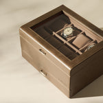 The TAWBURY Bayswater 8 Slot Watch Box with Storage in taupe features a glass top, plush watch pillows for displaying two wristwatches, and extra compartments for organized watch storage.