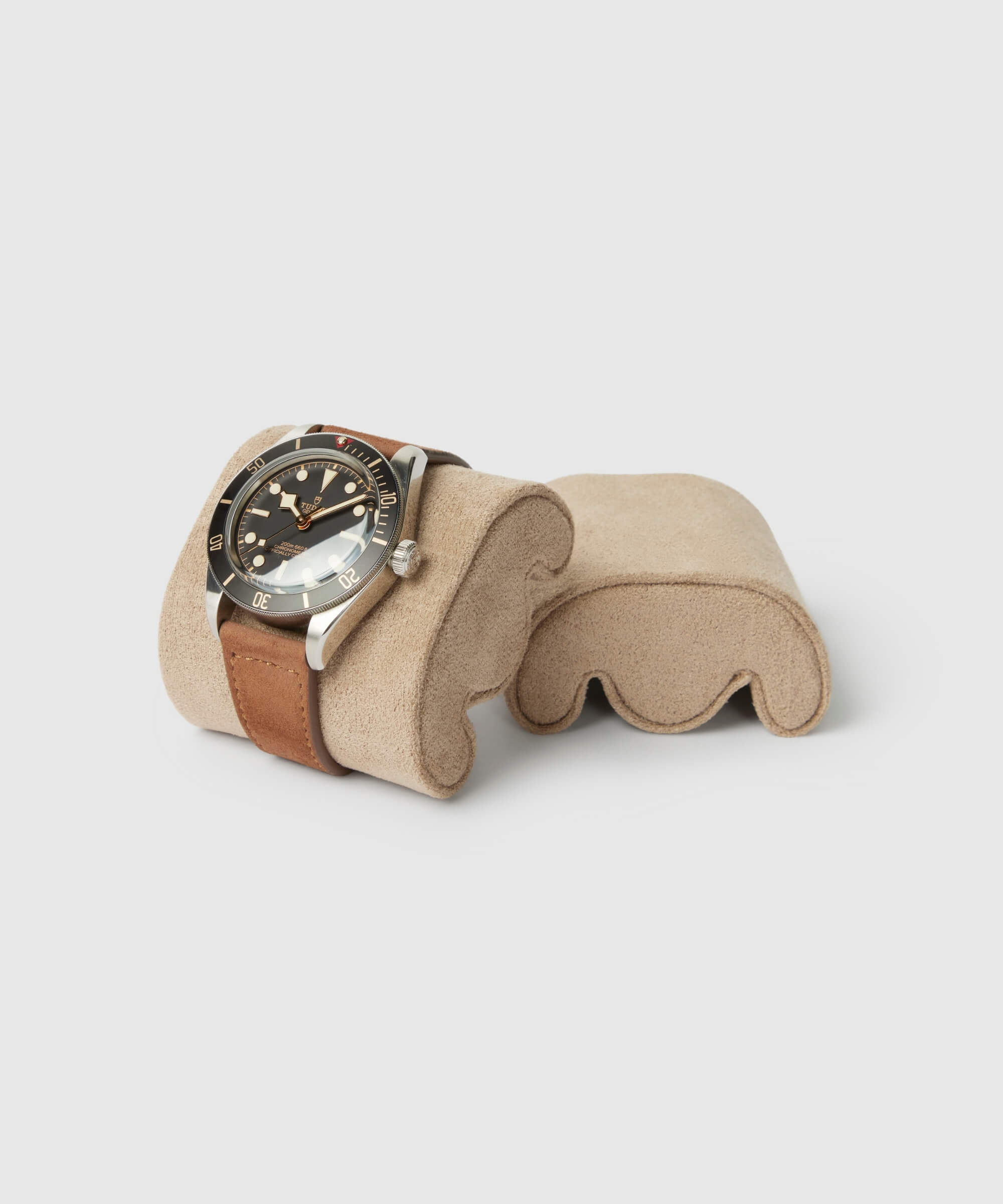 A wristwatch with a brown leather strap and black dial displayed on a beige cushioned Fraser Replacement Watch Case Pillows - X-Small - Taupe/Cream by TAWBURY.