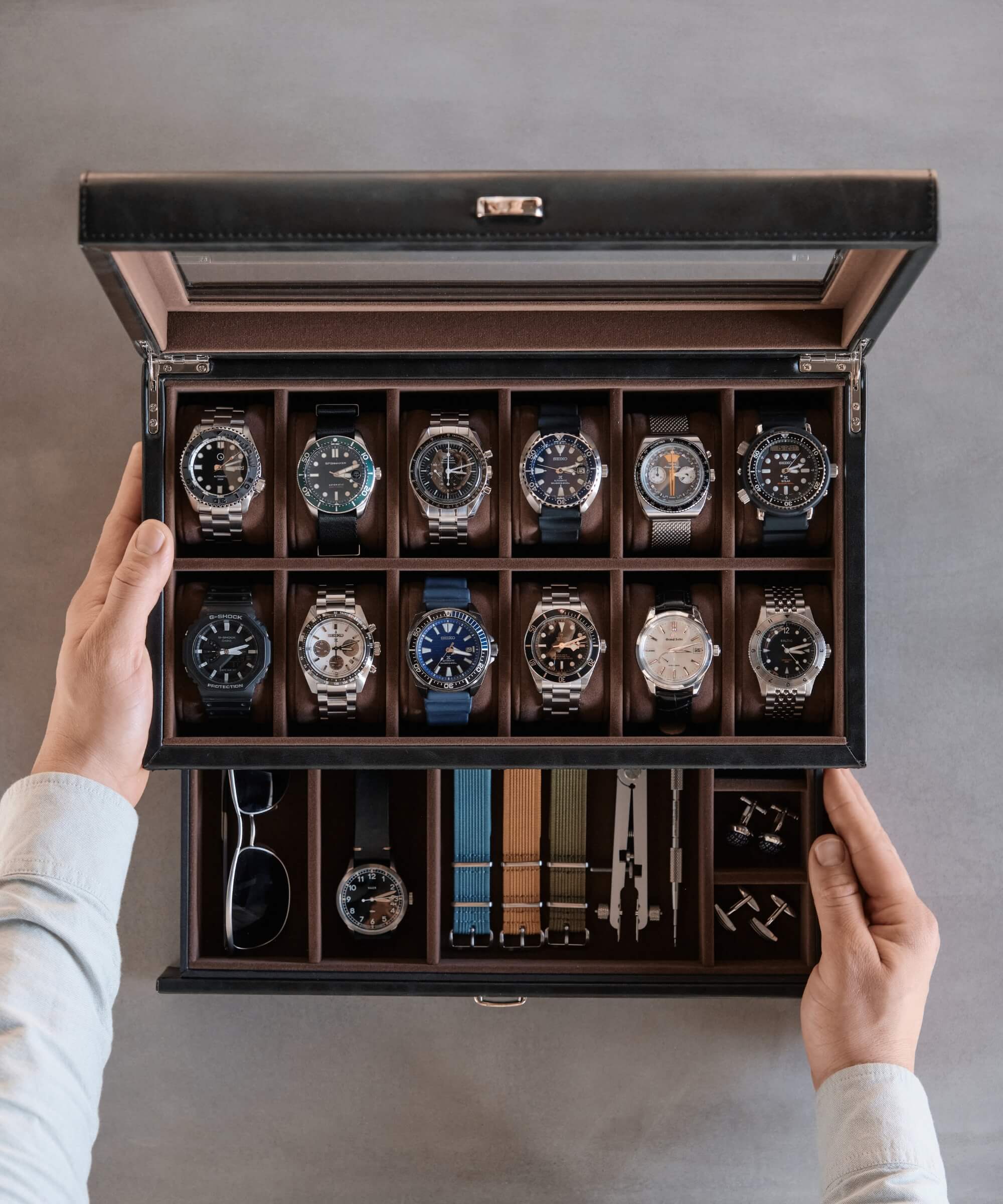 A person holding a Bayswater 12 Slot Watch Box with Drawer - Black from TAWBURY full of timepieces.