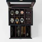 The TAWBURY Bayswater 6 Watch Jewelry Box in black/charcoal features a glass lid and displays six watches, cufflinks, rings, sunglasses, watch straps, a metal bracelet, and a pendant on a white background.