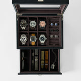 The TAWBURY Bayswater 6 Watch Jewelry Box in black/charcoal features a glass lid and displays six watches, cufflinks, rings, sunglasses, watch straps, a metal bracelet, and a pendant on a white background.