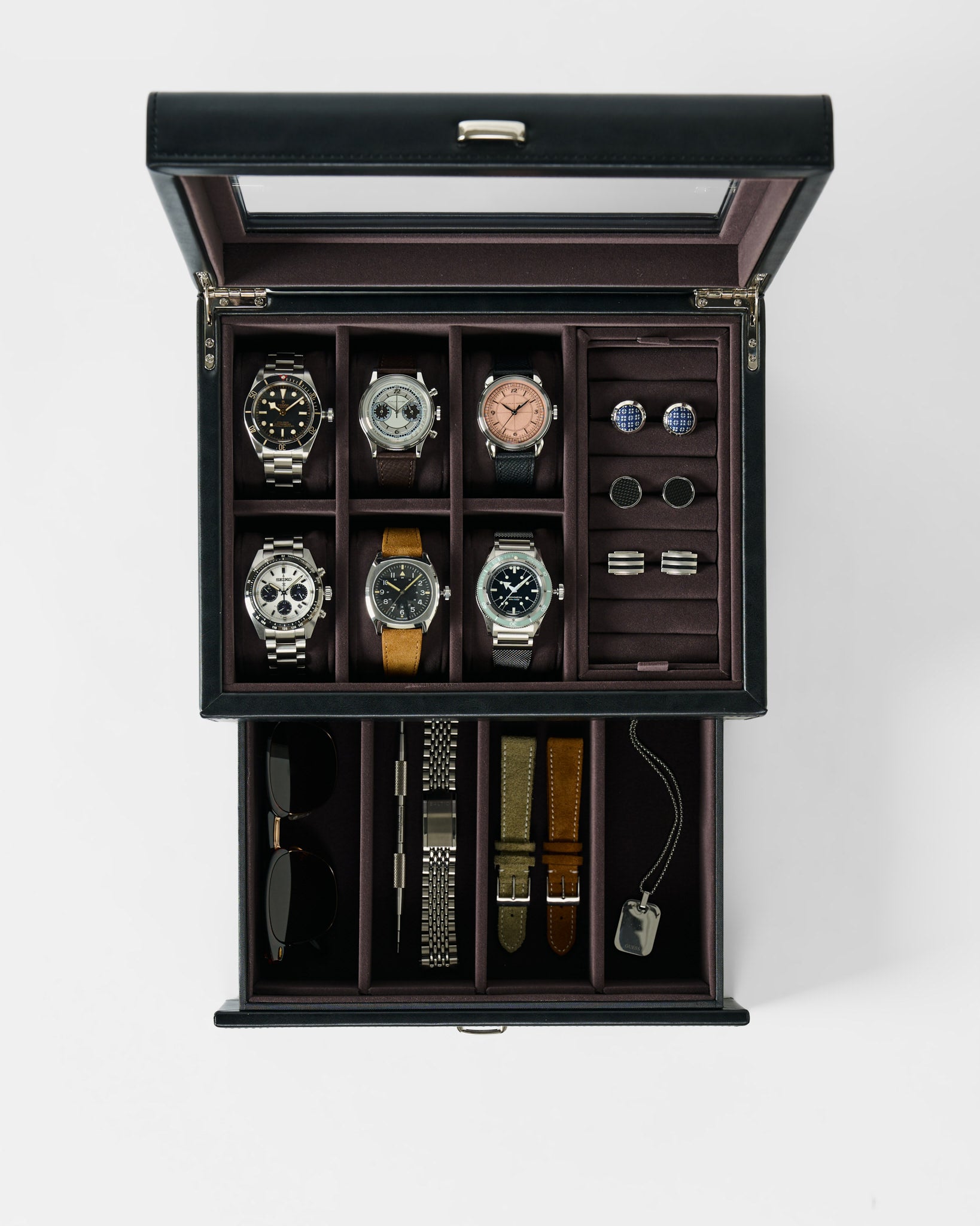 The TAWBURY Bayswater 6 Watch Jewelry Box in black/charcoal features a glass lid and displays six watches, cufflinks, rings, sunglasses, watch straps, a metal bracelet, and a pendant on a white background.