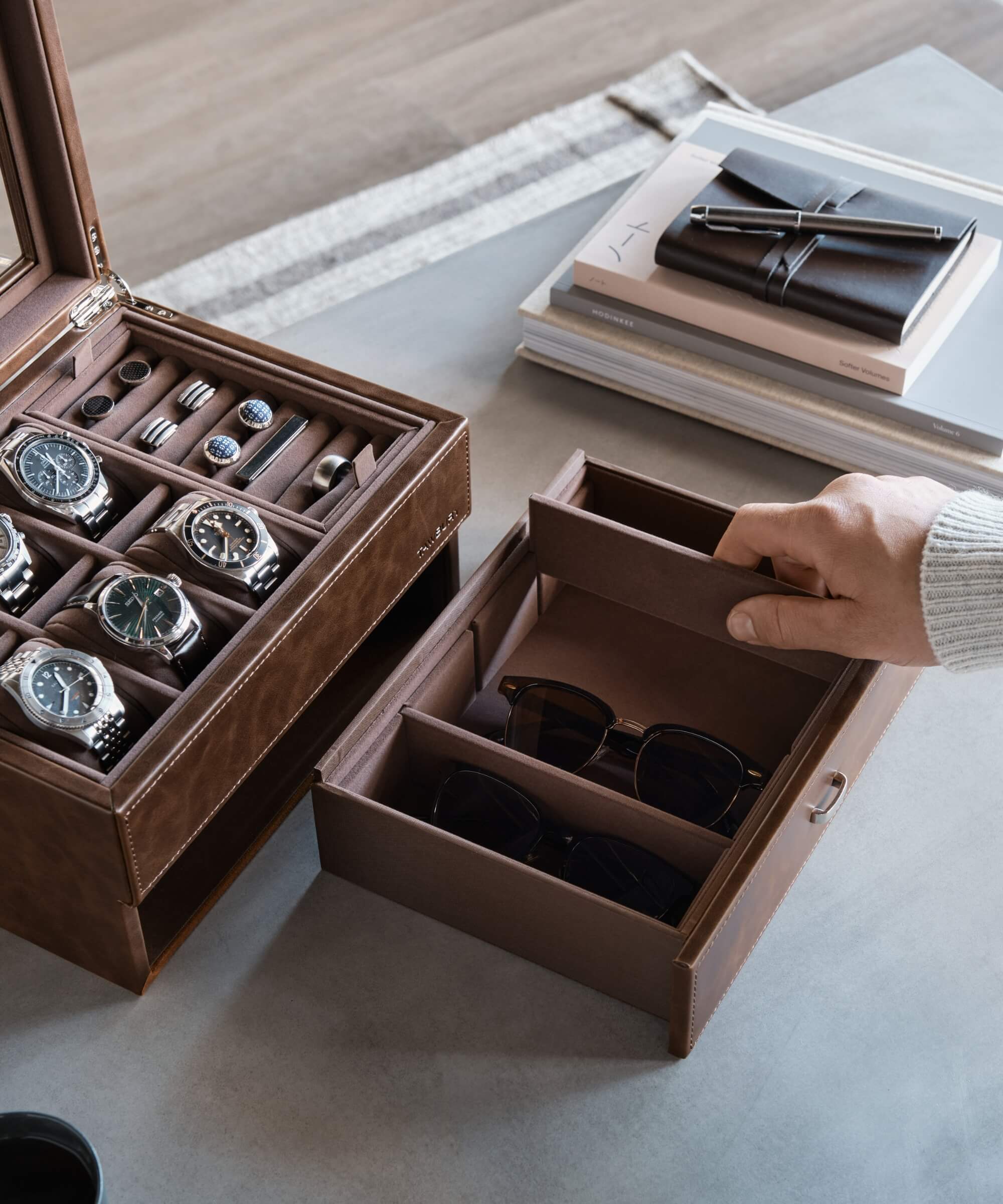 A watch enthusiast is showcasing their TAWBURY Bayswater 6 Watch Jewellery Box - Brown, carefully cradling the timepiece within the elegant wooden box wrapped in luxurious vegan leather.