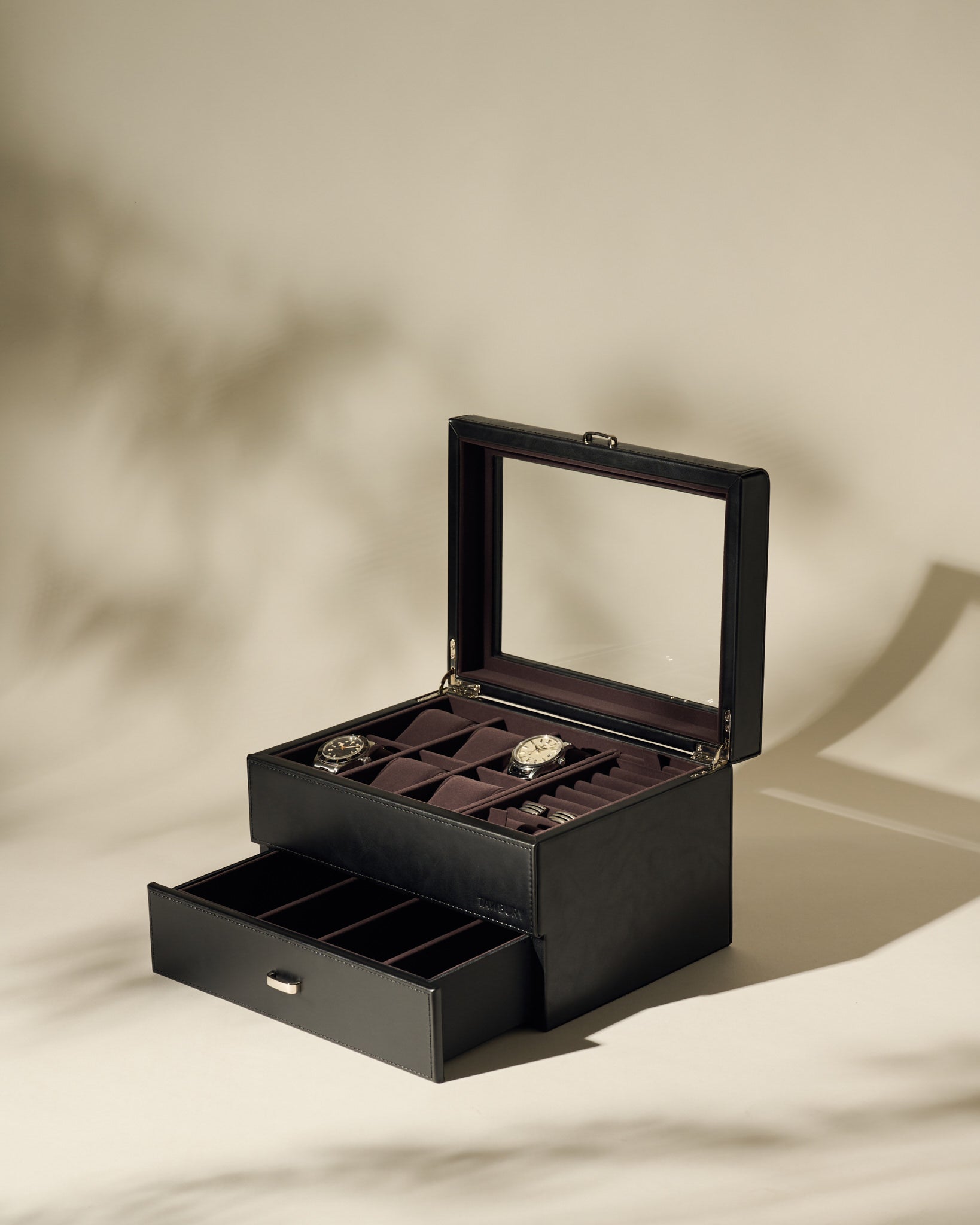 The TAWBURY Bayswater 6 Watch Jewelry Box in Black/Charcoal features a glass lid and an open display with two watches in separate compartments, plus a lower drawer with additional empty storage sections.