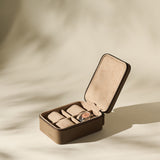 The TAWBURY Fraser 4 Watch Case in taupe is shown open on a beige surface, with multiple compartments visible and one securing a wristwatch.