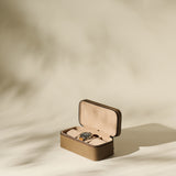 The TAWBURY Fraser 3 Watch Case in taupe, shown open with a wristwatch inside, offers stylish travel storage for your timepieces against a softly lit, neutral backdrop with gentle shadows.