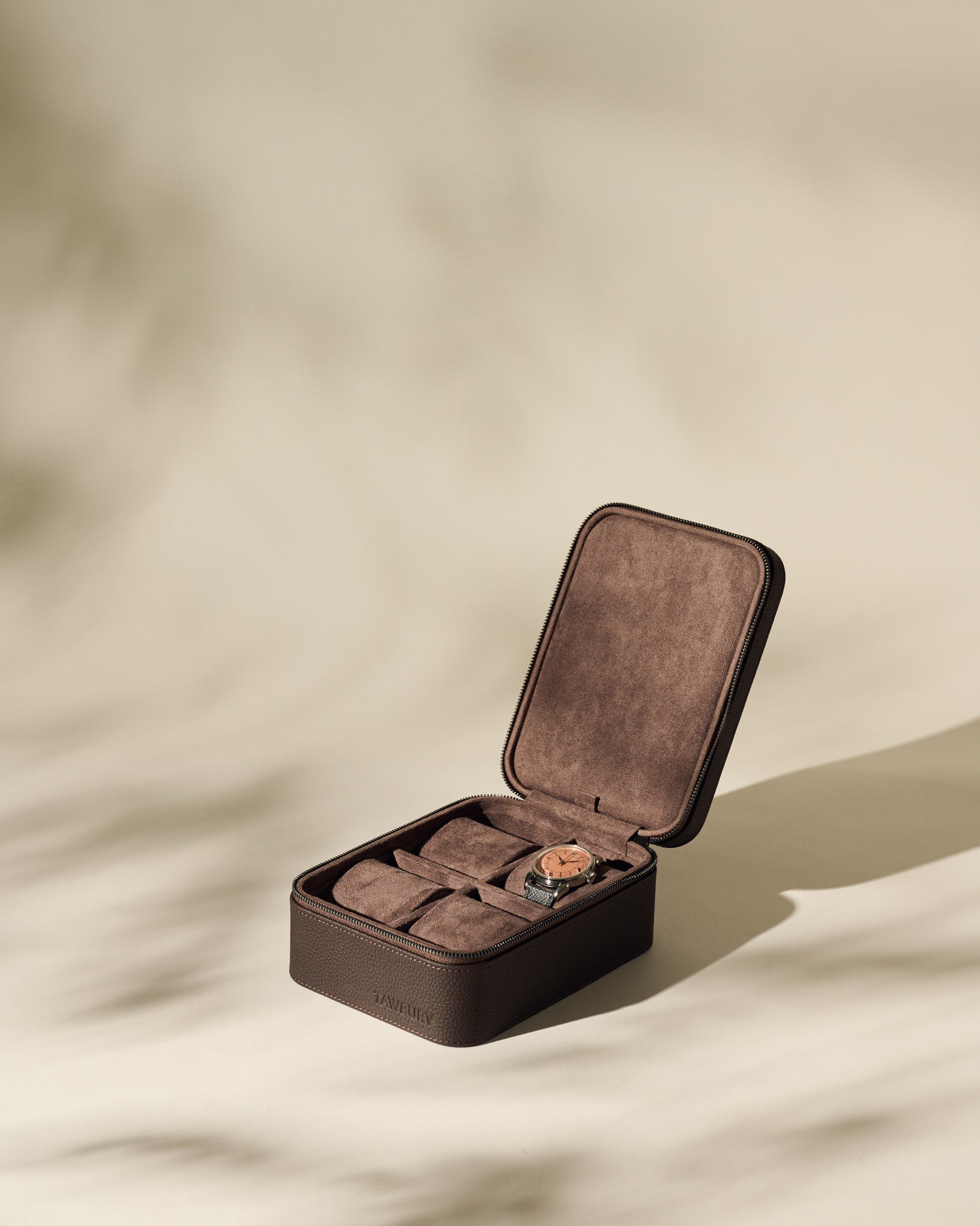 The TAWBURY Fraser 4 Watch Case - Brown features four compartments and brown suede lining, shown open with a watch inside—ideal for keeping your timepieces organized and protected at home or while traveling.