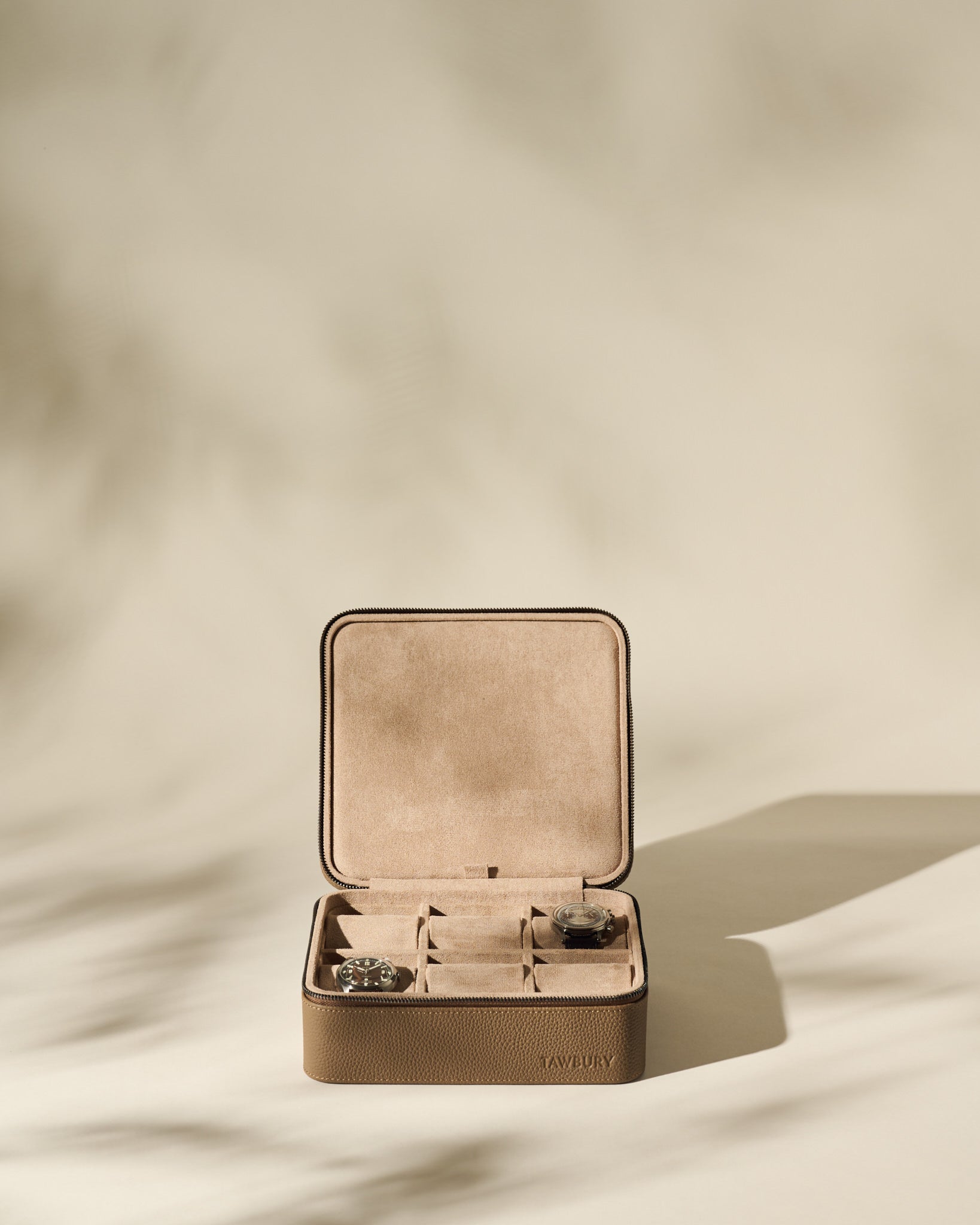 The TAWBURY Fraser 6 Watch Case in taupe, shown open with two watches inside and two empty compartments, offers a stylish storage solution for your collection against a neutral backdrop.