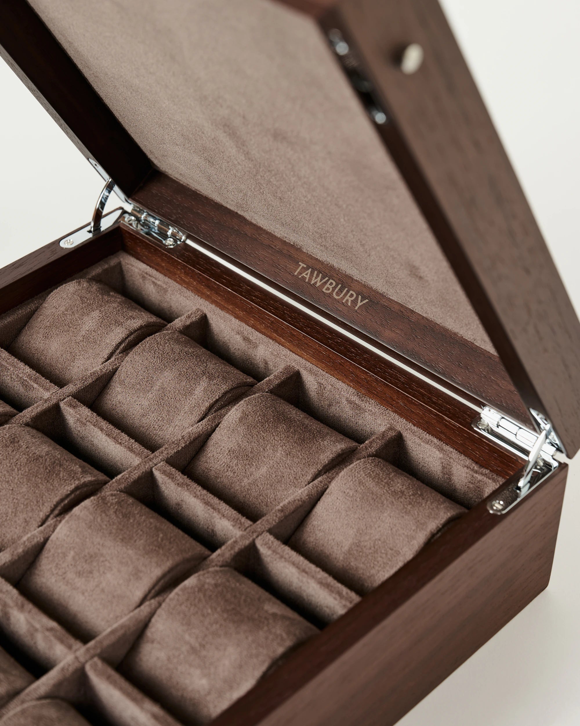 The TAWBURY Grove 12 Slot Wooden Watch Box features a dark walnut finish, solid hinged lid, soft brown interior with 12 cushioned compartments, and "TAWBURY" elegantly engraved inside the lid.