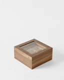 The TAWBURY Grove 6 Slot Wooden Watch Box in light walnut wood features a glass lid and divided compartments—an elegant display case for watch enthusiasts, set against a plain white background.
