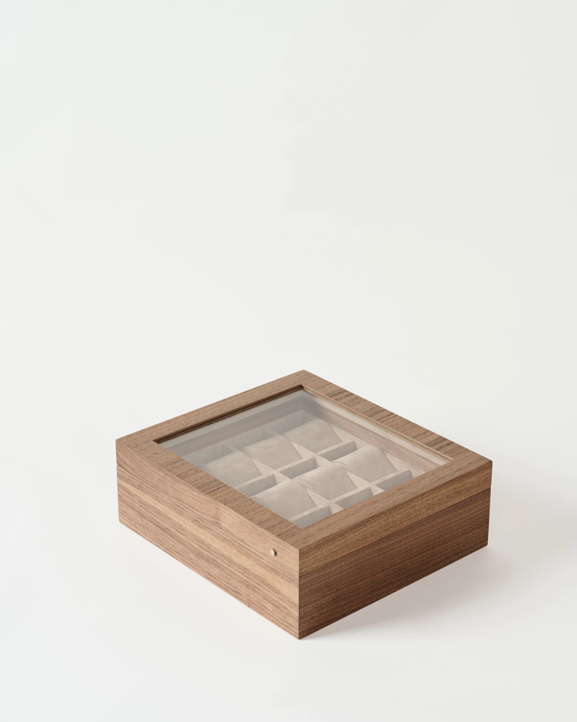The TAWBURY Grove 12 Slot Wooden Watch Box in light walnut with a glass lid is shown on a plain white background, featuring multiple compartments for storing watches.