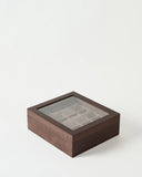 The TAWBURY Grove 12 Slot Wooden Watch Box in dark walnut wood features a glass lid, offering elegant storage and display for watches.