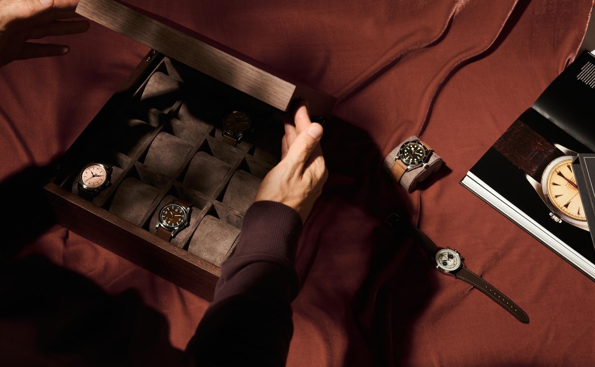 Person selecting a watch from a wooden watch box on a red surface