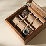 The TAWBURY Grove 6 Slot Wooden Watch Box in light walnut wood features a glass lid, two cushioned watch slots, and two empty beige suede-lined compartments—an elegant storage choice for watch enthusiasts.