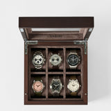 The TAWBURY Grove 6 Slot Wooden Watch Box in dark walnut features a glass lid and six cushioned compartments for neatly organizing your wristwatches in style.