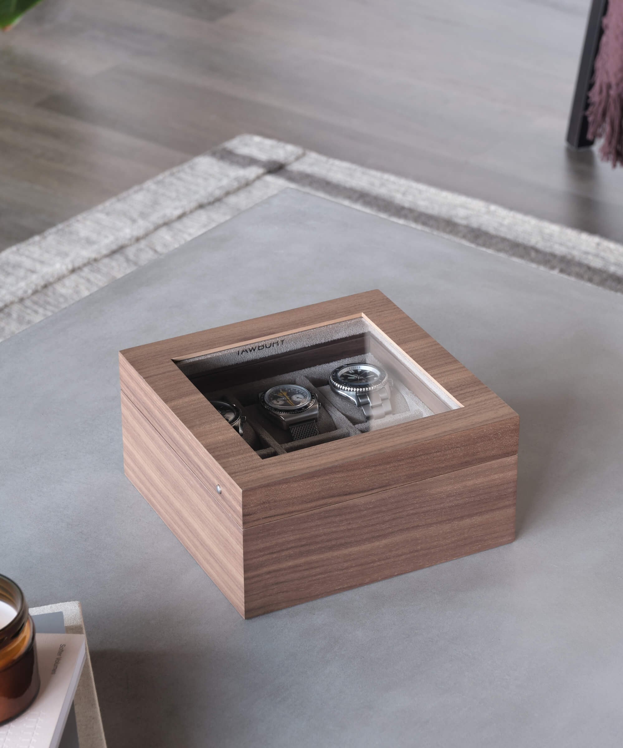 A TAWBURY Grove 6 Slot Watch Box with Glass Lid - Walnut on a table next to a coffee table, perfect for watch enthusiasts.