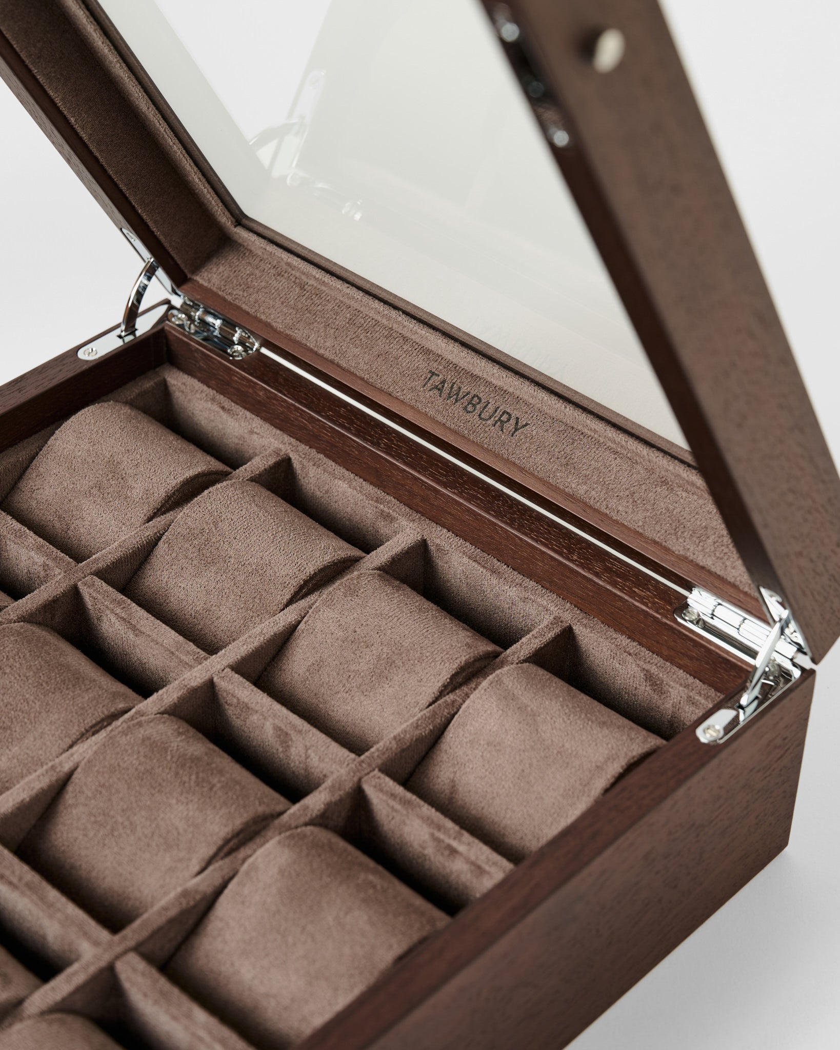 The TAWBURY Grove 12 Slot Wooden Watch Box in dark walnut features a glass lid, twelve suede-lined compartments, and an engraved logo inside—a stylish storage solution for watch collectors.