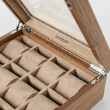 The TAWBURY Grove 12 Slot Wooden Watch Box features a light walnut finish, glass lid, beige suede interior, and multiple compartments for storing watches, with the TAWBURY logo inside the lid.