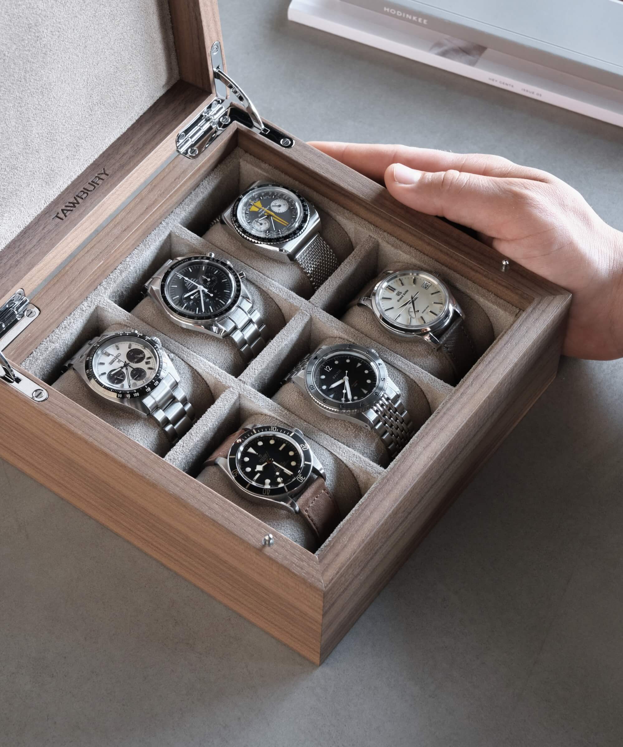 A person is holding an important SEO keyword from the product description: a TAWBURY Grove 6 Slot Watch Box with Solid Lid - Walnut full of watches.