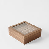 The TAWBURY Grove 12 Slot Wooden Watch Box in classic walnut wood features a glass lid and interior compartments, elegantly organizing multiple watches and showcased on a white background.