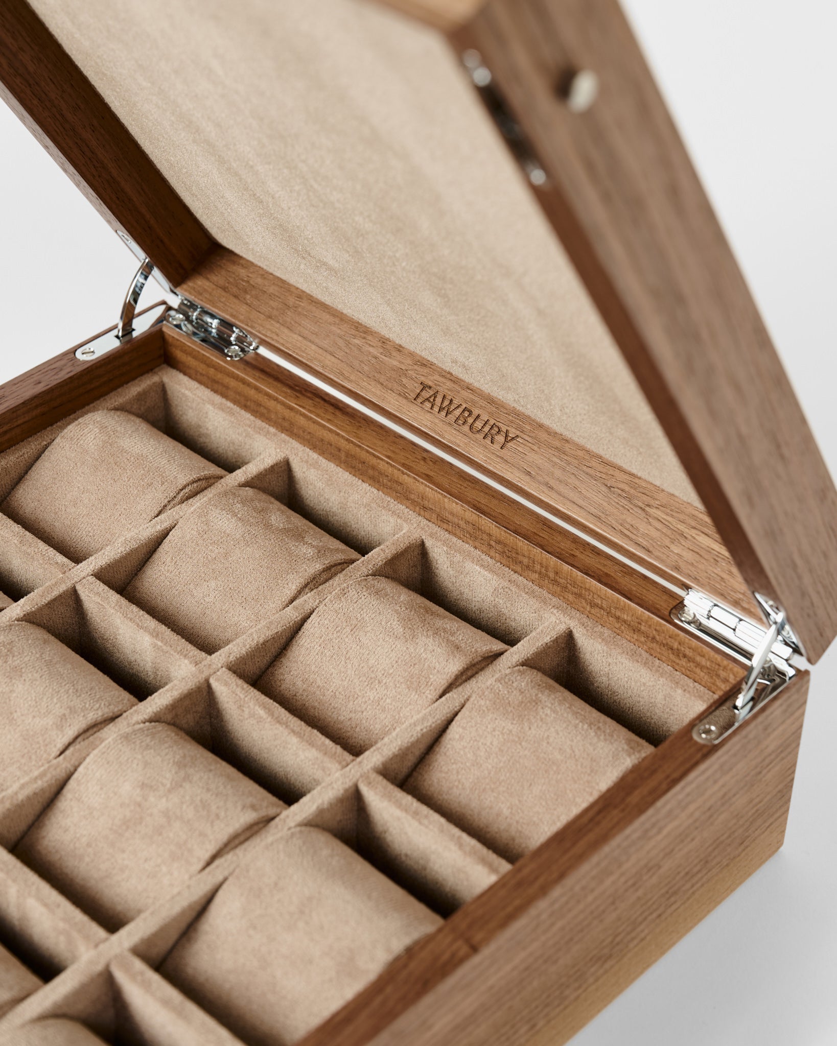 The TAWBURY Grove 12 Slot Wooden Watch Box, crafted from light walnut wood with a solid hinged lid and 12 padded compartments, is perfect for collectors; the TAWBURY logo is elegantly engraved inside the lid.