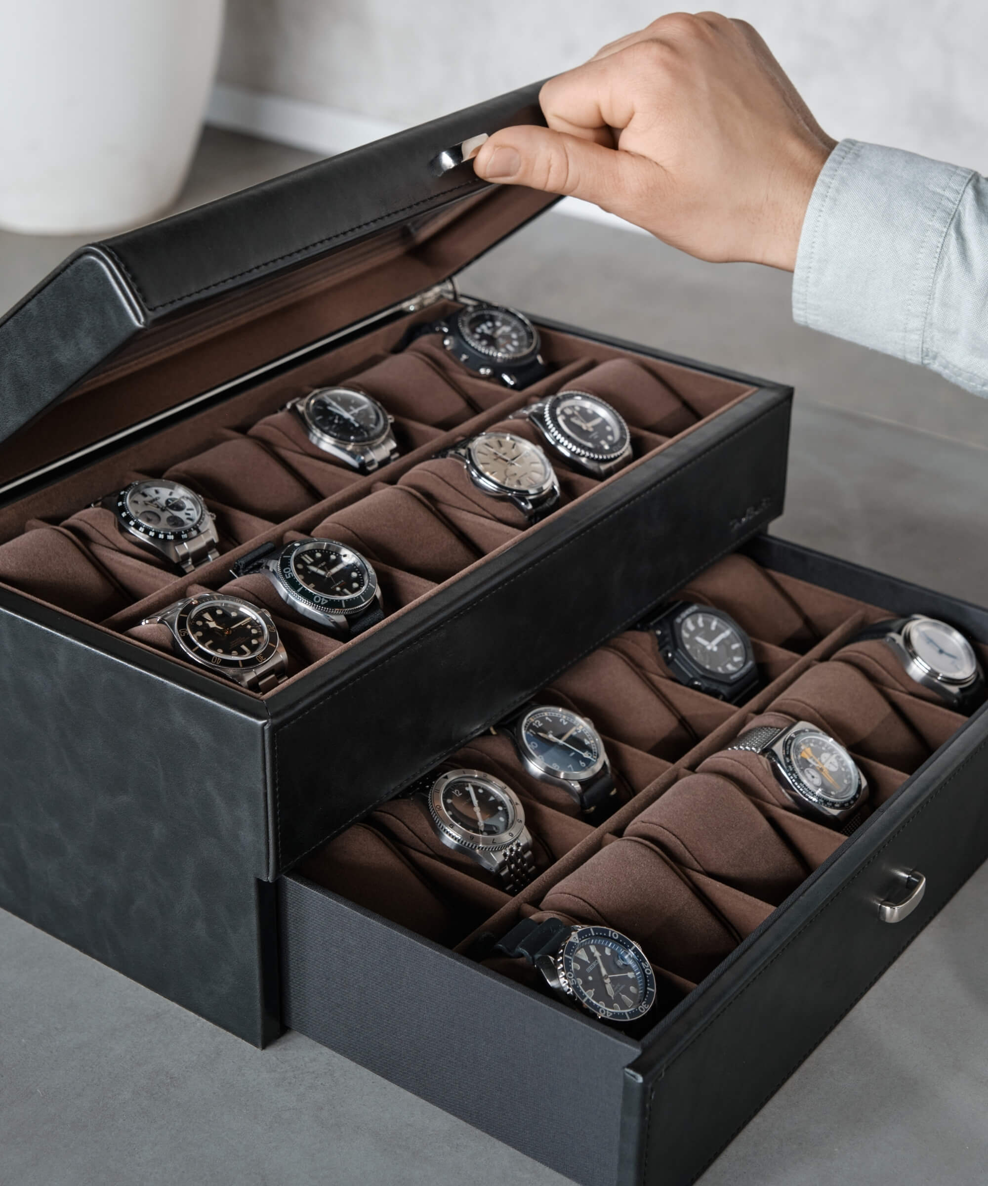 A man is using a TAWBURY Bayswater 24 Slot Watch Box with Drawer - Black to organize and protect his collection of watches.