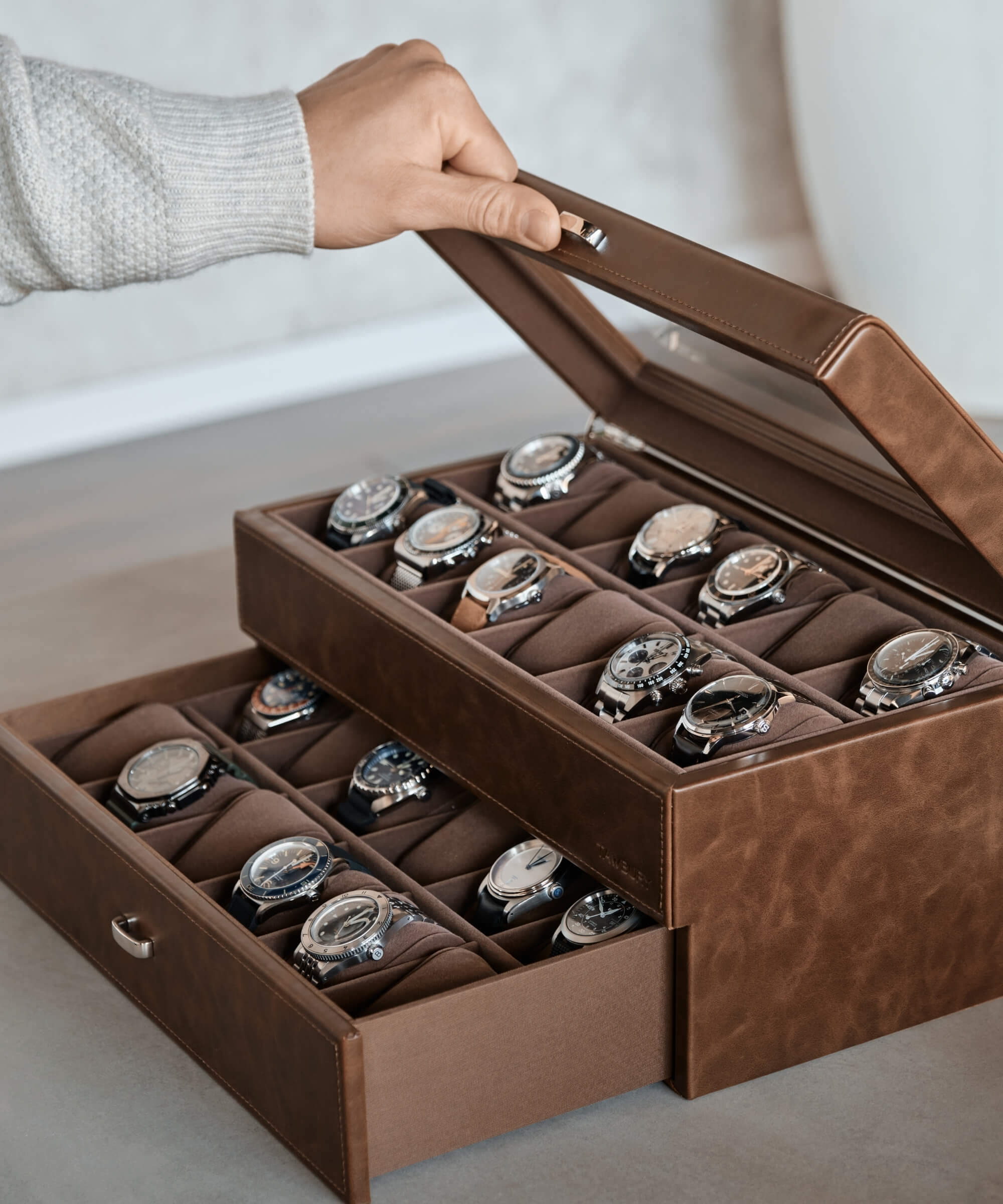 A watch enthusiast is opening a TAWBURY Bayswater 24 Slot Watch Box with Drawer - Brown full of timepieces.