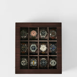 The TAWBURY Grove 12 Slot Wooden Watch Box in dark walnut wood features a glass lid and showcases twelve wristwatches, each in its own compartment—an elegant storage solution for collectors.