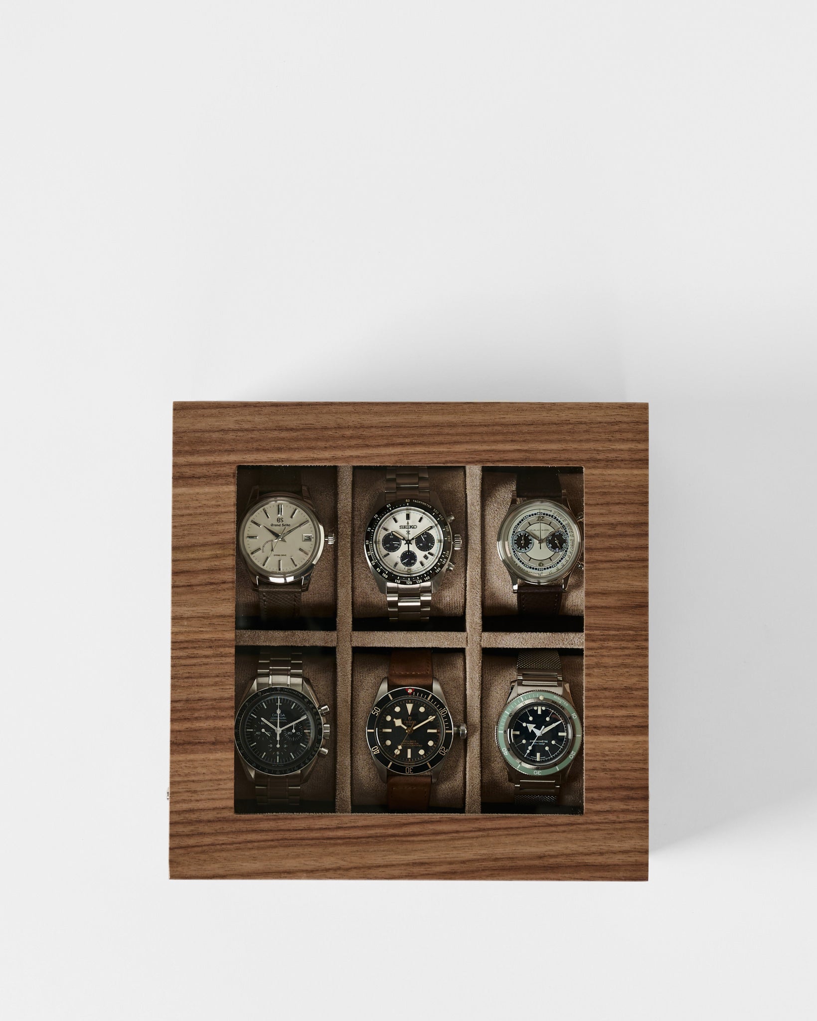 The TAWBURY Grove 6 Slot Wooden Watch Box in light walnut wood features a glass lid and showcases six wristwatches, elegantly displayed on a white background.