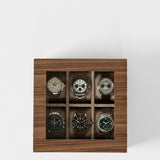 The TAWBURY Grove 6 Slot Wooden Watch Box in light walnut wood features a glass lid and showcases six wristwatches, elegantly displayed on a white background.